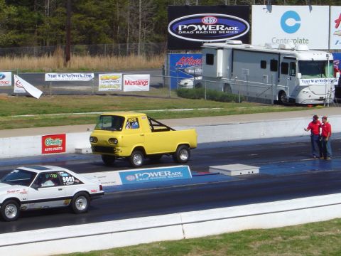 1986 Ford Bronco - A yellow 1961 Ford Econoline pickup truck races down a drag strip next to a white car.