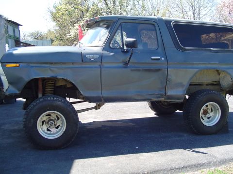 1979 Ford Bronco - Side view of a lifted Ford Bronco with off-road tires, showing body damage.