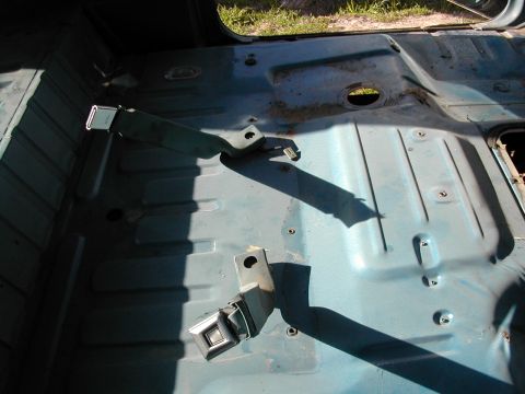 1981 Ford Bronco - The bare metal floor of a vehicle interior, showing seatbelt mounting points and some surface rust.