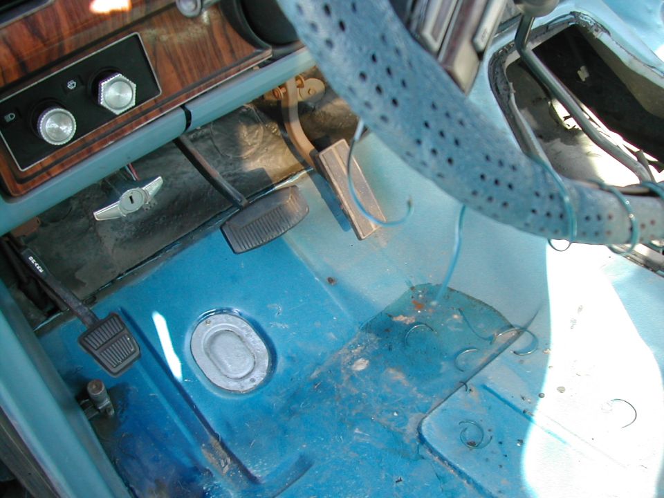 Vehicle interior showing floor pedals, steering column, and dashboard controls