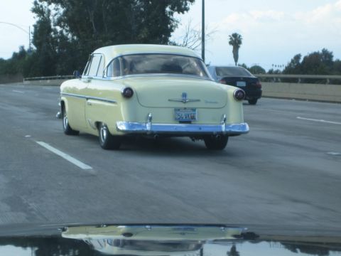 1968 Ford Mustang - A yellow 1954 sedan is seen from behind on the highway, with another car in the background.