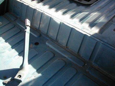 1981 Ford Bronco - The interior floor of a vehicle shows a seat belt anchor and ribbed metal construction.