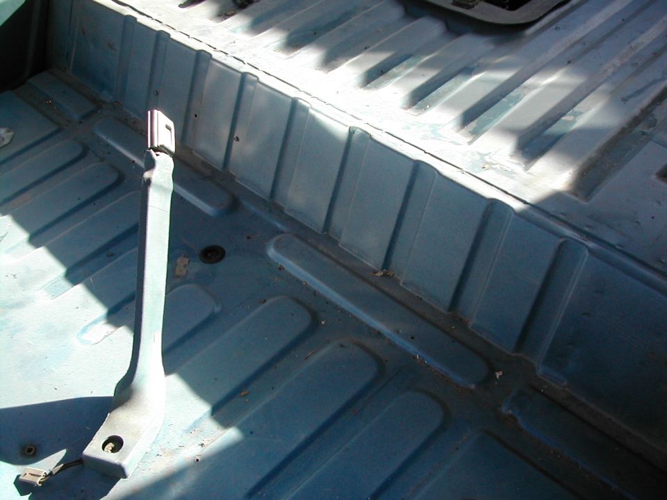 Interior floor of a vehicle with blue painted metal and seat belt anchor