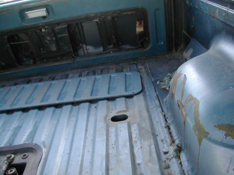 1981 Ford Bronco - The interior of a truck bed shows wear and tear, with exposed metal and insulation.