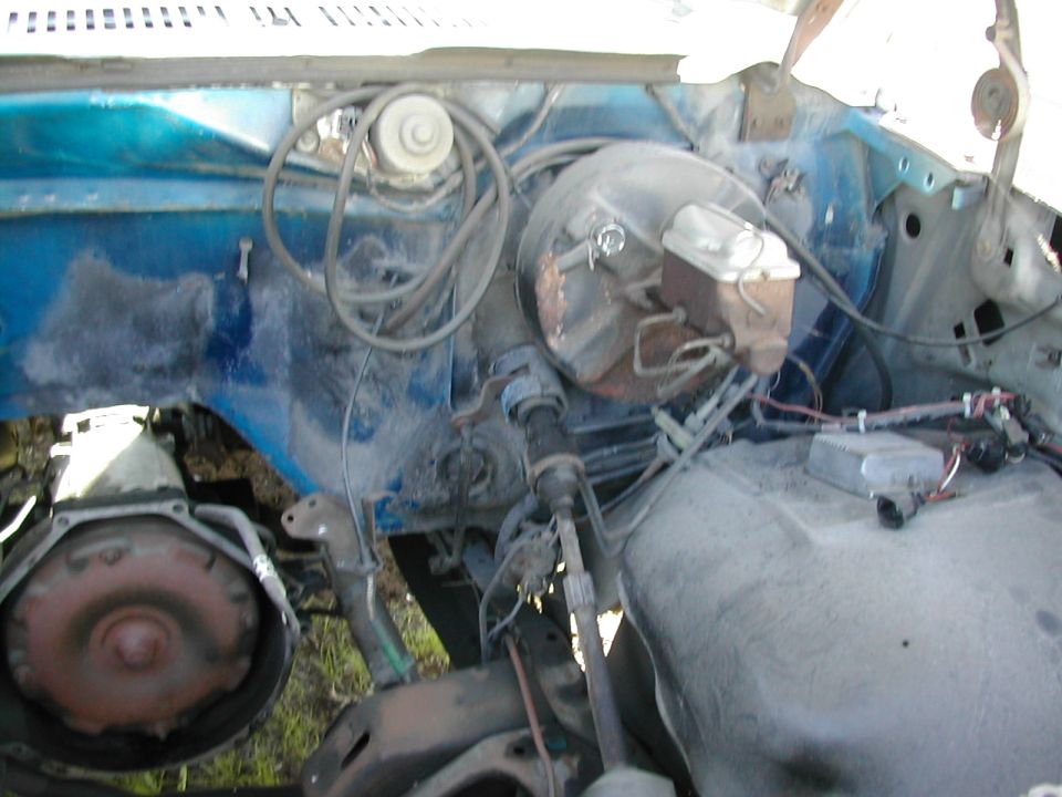 Close-up of a vehicle's engine bay, showing the brake booster, master cylinder, and transmission bell housing
