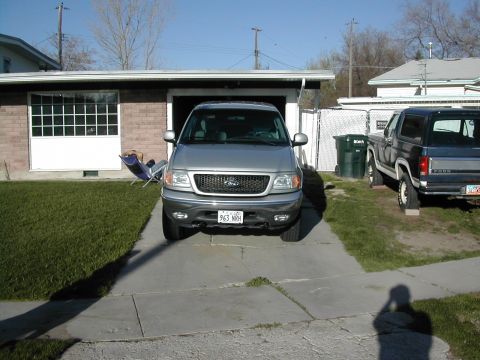 1981 Ford Bronco - Two SUVs are parked in a driveway in front of a garage and house.