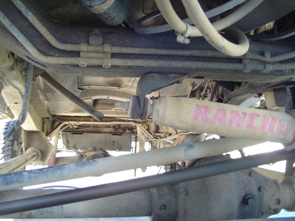 Underside view of a vehicle's suspension with a Rancho shock absorber visible. Some hoses and frame components are also in the shot
