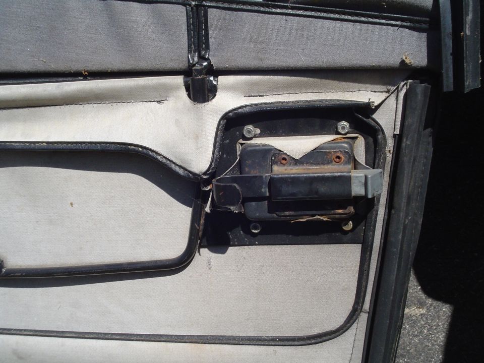 Close-up of a vehicle's interior door latch mechanism, showing screws and black plastic parts