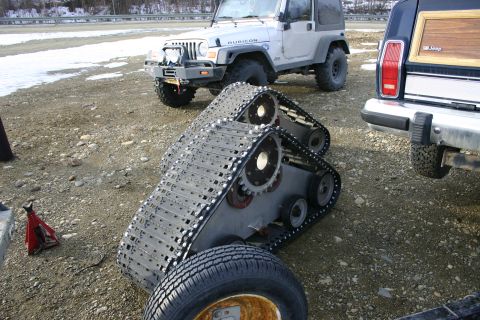 2003 Jeep TJ - A silver 2003 Jeep Wrangler is equipped with tracks, parked on a gravel lot next to a Jeep Cherokee.