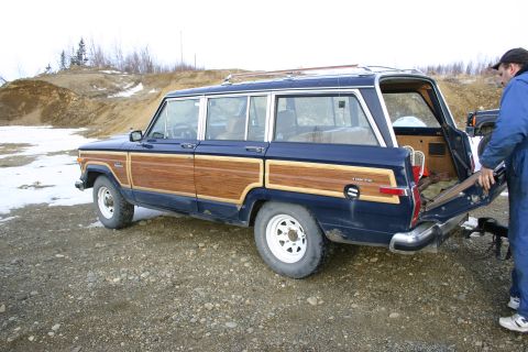 2003 Jeep TJ - A blue Jeep Grand Wagoneer with wood paneling is parked outdoors, with its rear hatch open.