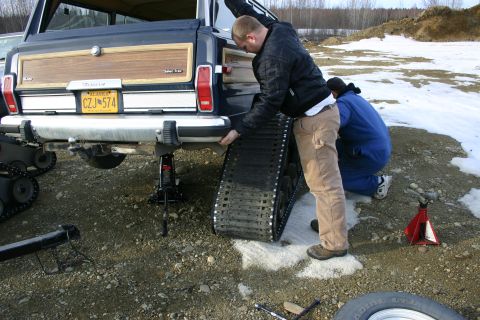 2003 Jeep TJ - Attaching snow tracks to a Jeep Grand Wagoneer in a snowy, outdoor setting.