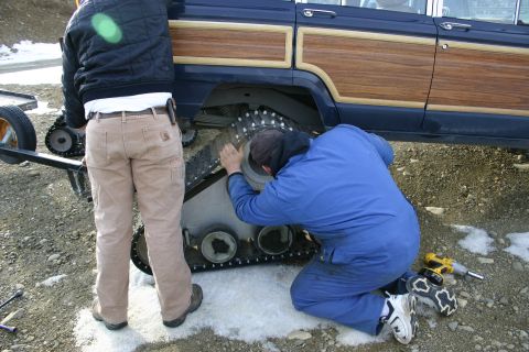 2003 Jeep TJ - Mechanics adjust snow tracks on a vintage Jeep Grand Wagoneer.
