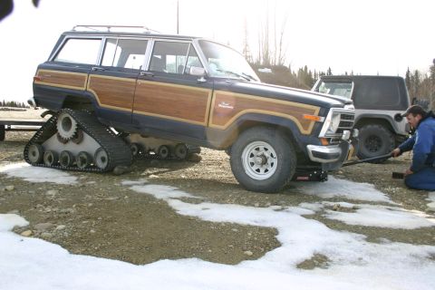 2003 Jeep TJ - A modified Jeep Grand Wagoneer, likely from the 1980s, is equipped with tank tracks instead of wheels, with a Jeep Wrangler visible behind…