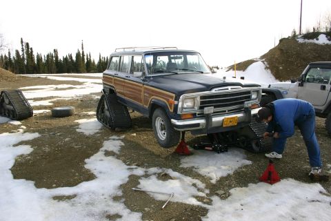 2003 Jeep TJ - A person works on a Jeep Grand Wagoneer equipped with snow tracks, with another Jeep visible in the background.