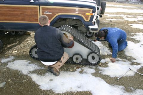 2003 Jeep TJ - Two men work on attaching tank tracks to a Jeep Grand Wagoneer with wood paneling.