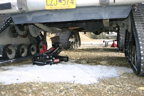 2003 Jeep TJ - A vehicle equipped with tracks is shown being lifted by a jack, with a yellow license plate visible above.