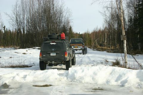 2003 Jeep TJ - Two SUVs navigate a snow-covered forest trail, one with a roof rack and gas can.