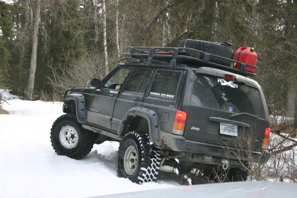 Black Jeep Cherokee XJ with roof rack and gas can driving in snow