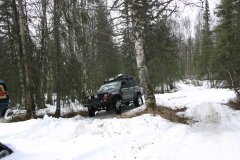 2003 Jeep TJ - A Jeep Cherokee XJ navigates a snowy forest trail, with another vehicle partially visible.