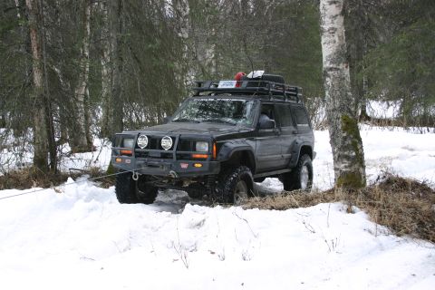 2003 Jeep TJ - A black Jeep Cherokee XJ is stuck in the snow and being pulled by a cable in a wooded area.