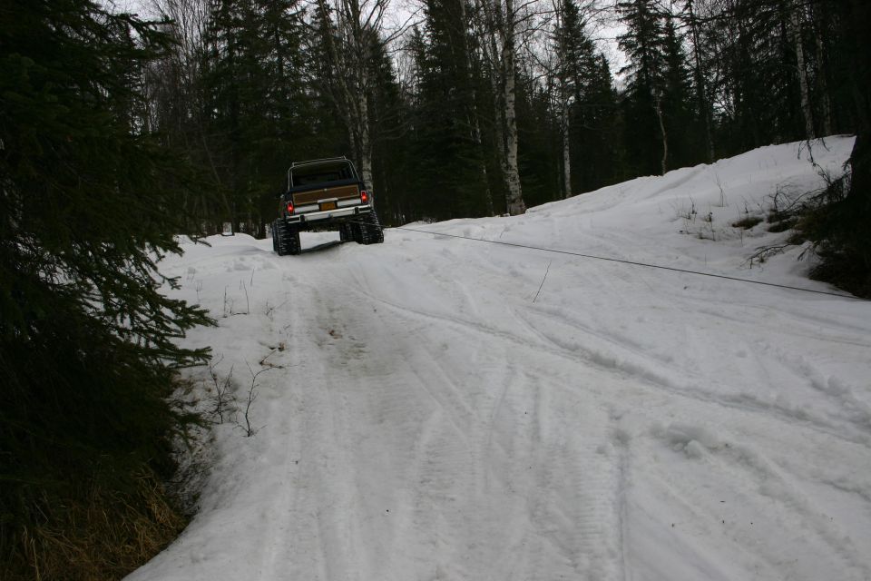 Brown SUV with large tires being towed up a snowy hill by a cable