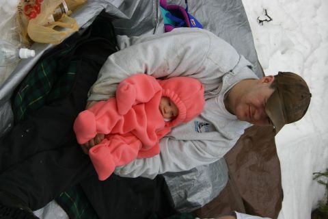 2003 Jeep TJ - A man and a baby are resting together on a tarp, with snow visible around them.