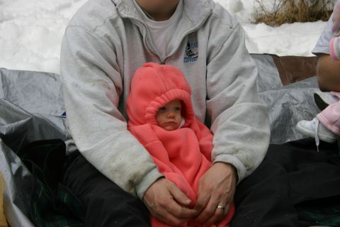 2003 Jeep TJ - A person holds a baby bundled in a pink hooded snowsuit while sitting outdoors in a snowy environment.