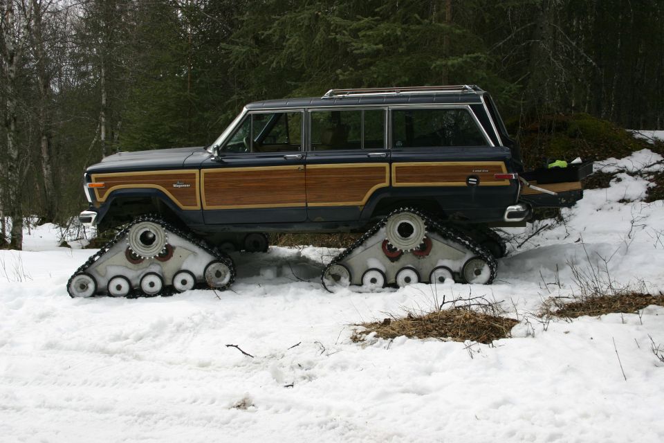 Jeep Grand Wagoneer with wood paneling, equipped with tank tracks instead of wheels, in a snowy wooded area