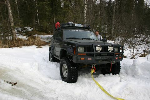 2003 Jeep TJ - A man watches as a black Jeep Cherokee XJ is stuck in deep snow, with a tow strap attached to its front.