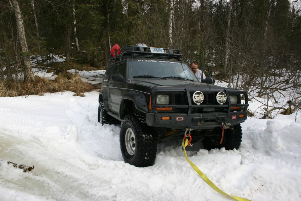 Black Jeep Cherokee XJ stuck in snow with a yellow tow strap attached to the front bumper
