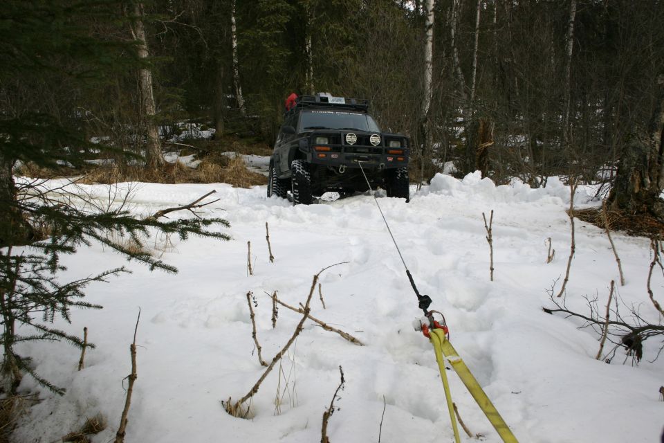 Black Jeep TJ in snow, front view, with winch line attached to a yellow strap