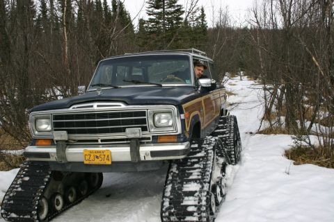 2003 Jeep TJ - A Jeep Grand Wagoneer equipped with tracks navigates a snow-covered path through a wooded area.