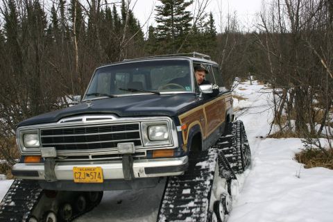 2003 Jeep TJ - A Jeep Grand Wagoneer equipped with tracks navigates a snowy trail through a wooded area.