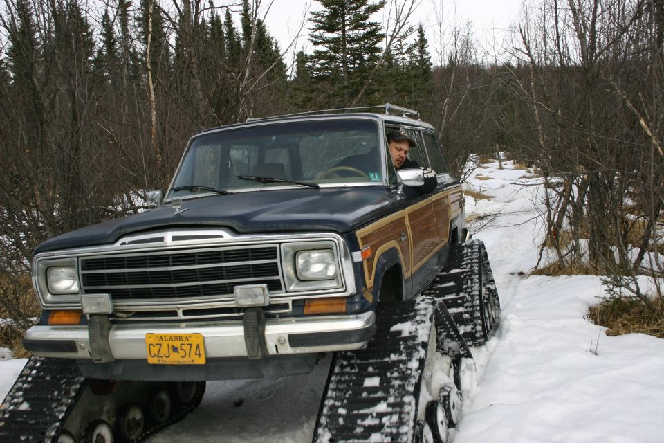 Dark blue Jeep Grand Wagoneer with wood paneling on tracks in snow, front 3/4 view