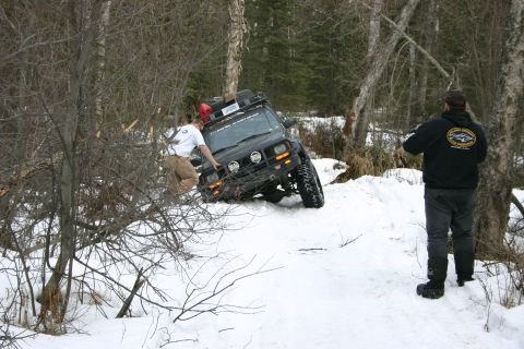 2003 Jeep TJ - A person attempts to push a Jeep Cherokee XJ out of a snowy trail while another person watches.