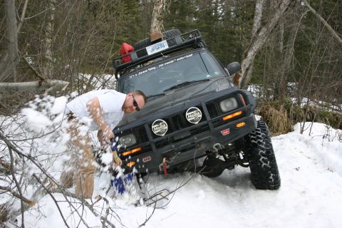 2003 Jeep TJ - A man shovels snow from around a modified Jeep Cherokee XJ in a snowy, wooded area.