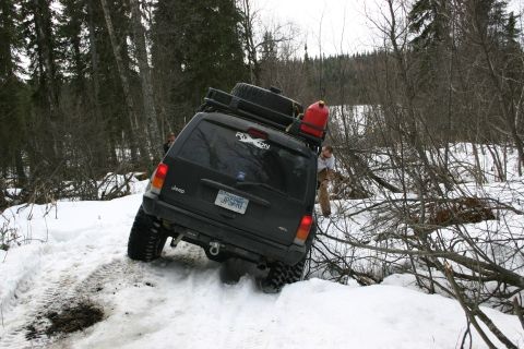 2003 Jeep TJ - A black Jeep Cherokee XJ navigates a snowy trail, equipped with a roof rack and a red gas can.