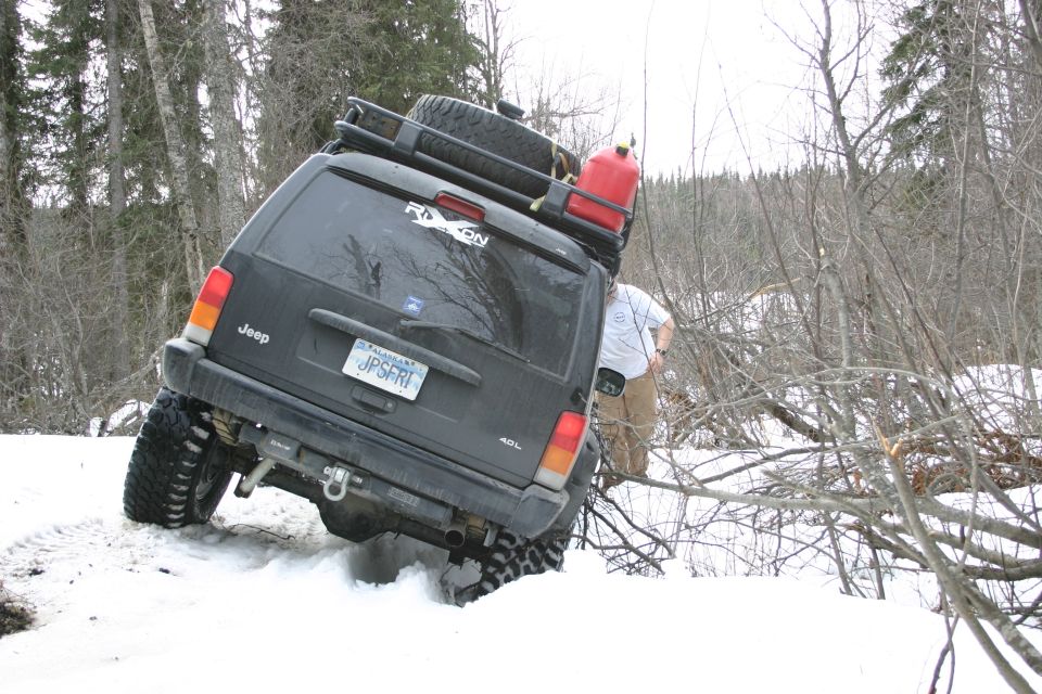 Black Jeep Cherokee XJ with roof rack and gas can stuck in snow, license plate JPSFRI