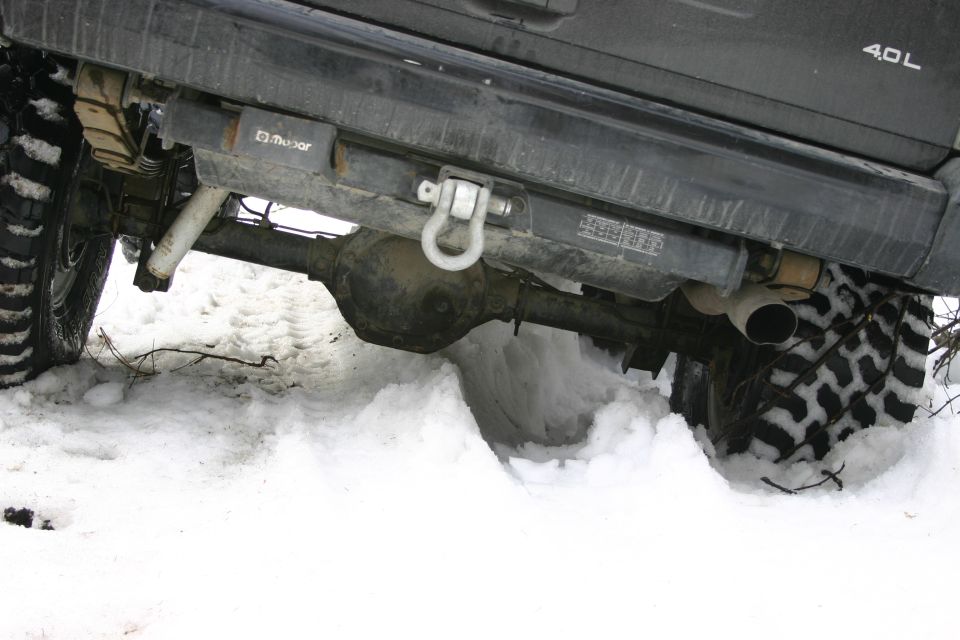 Rear axle, tow hitch, and tire of a Jeep partially buried in snow. "Mopar" logo visible on a component