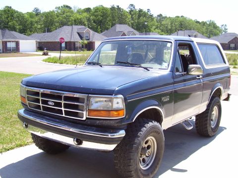 1992 Ford Bronco - Dark blue 1992 Ford Bronco with a white top is parked outside a suburban house.