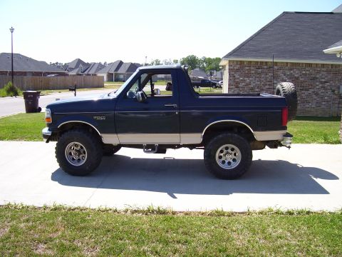 1992 Ford Bronco - This dark blue and tan Ford Bronco is parked in front of a brick house on a sunny day.