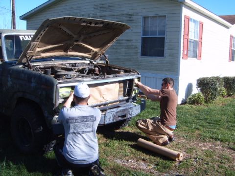 1988 Ford Bronco - Two men are working on the front end of a vintage Ford Bronco, with the hood open, in front of a mobile home.