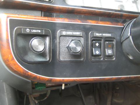 1990 Ford Bronco - vehicle's woodgrain-trimmed dash control panel shows knobs labeled Lights and Wipe-Wash plus rear-window switches.