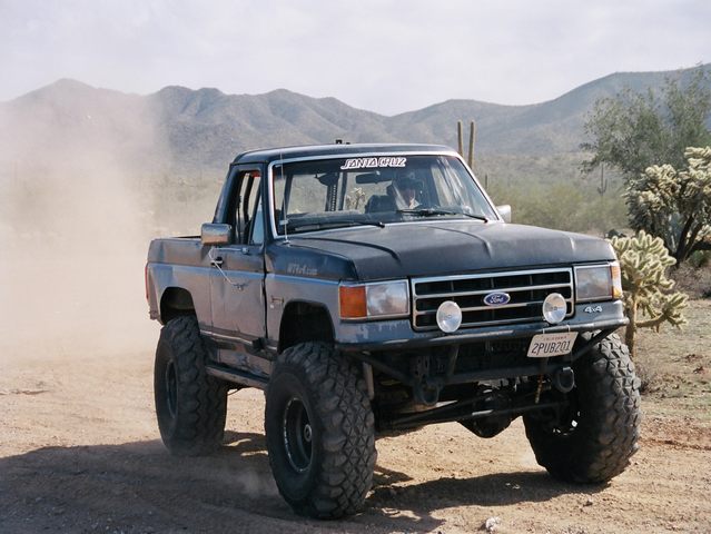 Lifted Ford pickup with Ford grille badge kicking dust on desert dirt road by mountains