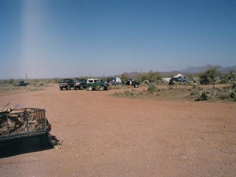 1989 Ford Bronco - A group of vehicles and camping equipment are gathered in a dry, arid landscape under a clear blue sky.