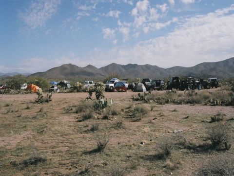 1989 Ford Bronco - A group of off-road vehicles and tents are set up in a desert area with mountains visible in the distance.