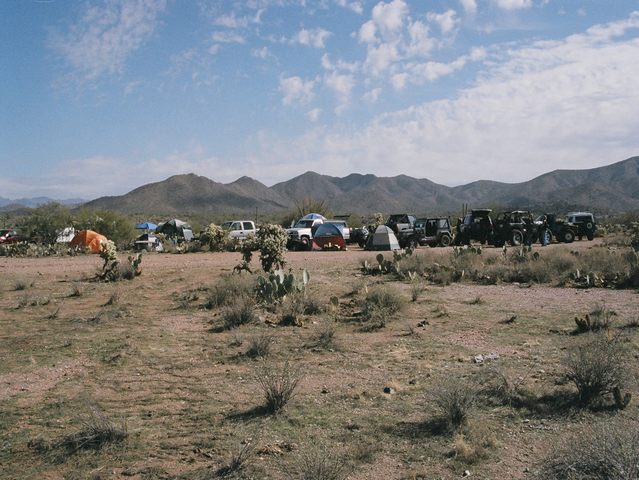 Row of 4x4s and tents at a desert off-road camp below mountains