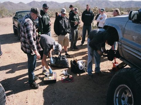 1989 Ford Bronco - A group of people gather in a desert landscape to work on the suspension of a lifted SUV.