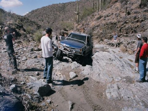 1989 Ford Bronco - A blue 1989 Ford Bronco tackles a challenging rocky trail in a desert landscape.