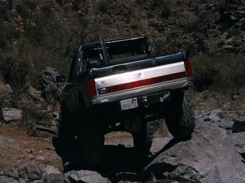 1989 Ford Bronco - 1989 Ford Bronco navigating a rocky off-road path in a desert landscape.